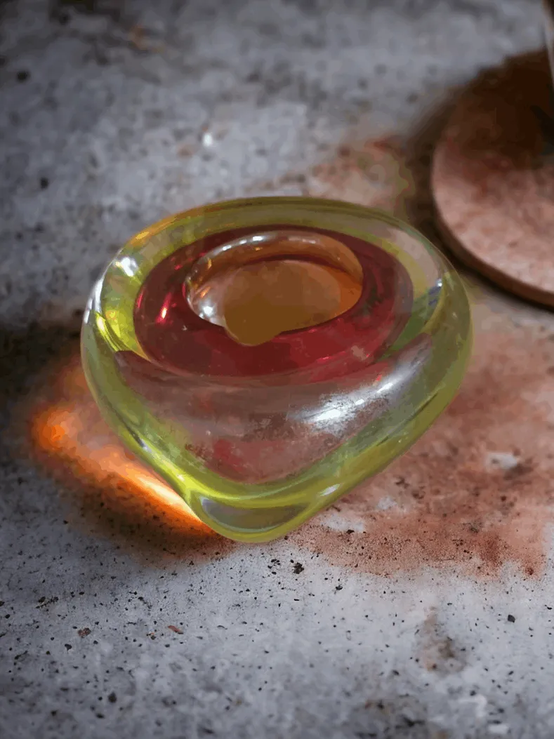 穆拉诺玻璃烟灰缸是一个精致的物品，展现了穆拉诺玻璃大师的优雅和技艺。每个烟灰缸都经过手工制作，代表着一个独特的作品，得益于在玻璃加工中使用的传统工艺。主要特点：材料和设计：这些烟灰缸采用吹制玻璃手工制作，可能具有圆形、几何形状或更复杂的设计，配有色彩斑斓的细节和透明效果。一些型号还包括马林花纹装饰、金银箔的使用以及能够 spectacular地捕捉光线的图案。颜色和风格：提供各种鲜艳的颜色或更为素雅的色调，通常伴随着渐变和透明效果，突显玻璃的美丽。有些作品装饰有抽象、花卉或艺术性的图案。功能性与美学：穆拉诺玻璃烟灰缸非常适合为任何环境增添一丝优雅，既是装饰元素，也是功能性物品。它是客厅、书房或休息室的理想装饰品，也代表着为喜爱高质量手工艺的人们准备的独特礼物。