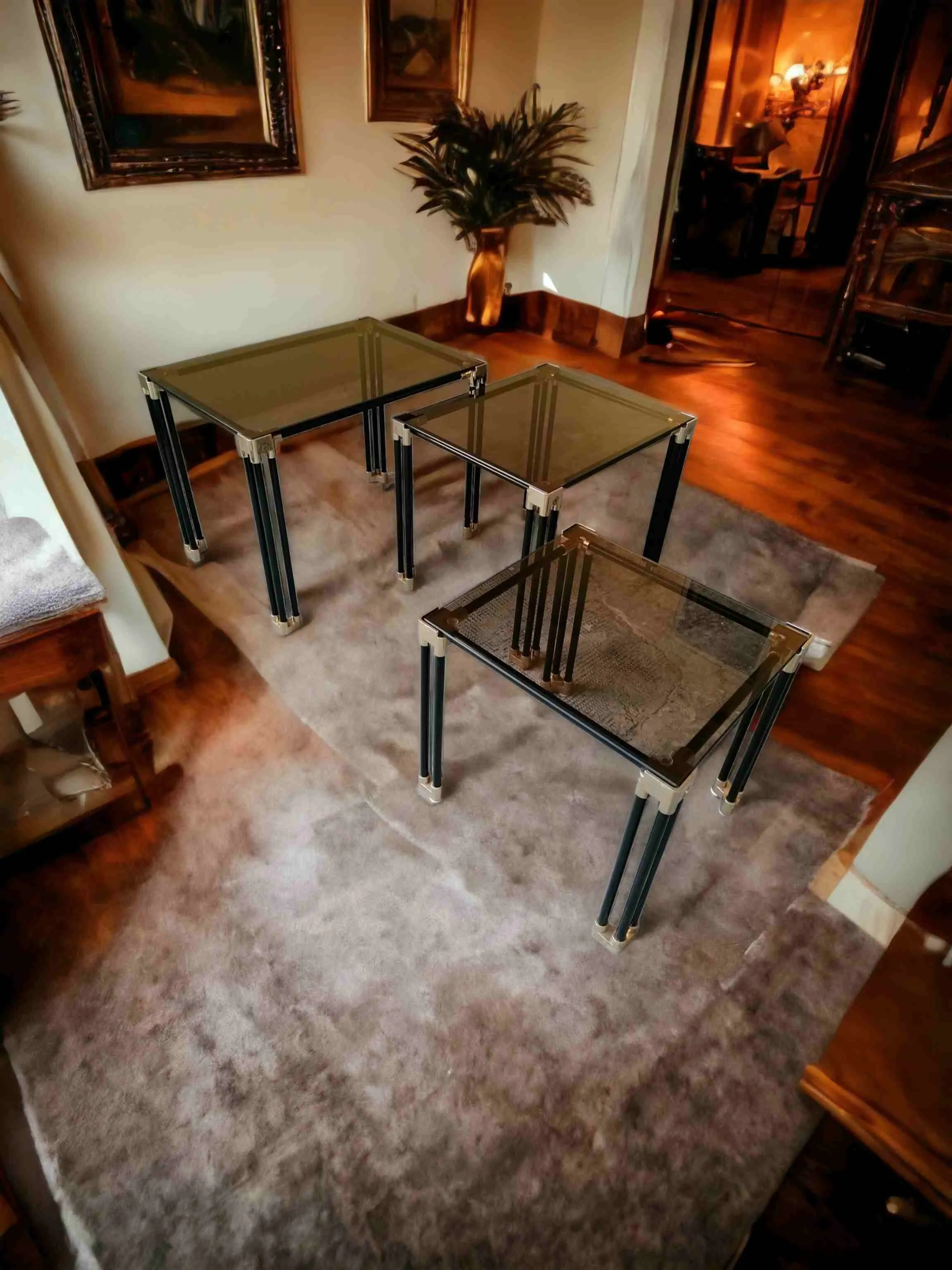 El conjunto de mesas auxiliares con vidrio ahumado es un set de elegantes mesas que expresan un diseño moderno y refinado. Cada pieza está caracterizada por tubos de metal pintados de negro, que aportan robustez y un toque industrial, y uniones de metal cromado o pulido que añaden un acento brillante y sofisticado. Características principales: Materiales de alta calidad: El vidrio ahumado agrega una elegancia discreta y hace que las mesas sean ideales para ambientes modernos o contemporáneos, creando un contraste con las estructuras oscuras de los tubos. Diseño armonioso: La combinación de tubos negros y detalles metálicos es perfecta para espacios minimalistas o industriales. Versatilidad: Las mesas pueden usarse juntas o por separado, ofreciendo flexibilidad para diferentes usos, como soporte para lámparas, libros u objetos decorativos. ¿Por qué elegirlas? Estas mesas son perfectas para quienes desean un complemento de decoración funcional y elegante. La transparencia del vidrio ahumado hace que el ambiente se vea más ligero, mientras que los detalles negros y metálicos aportan profundidad y modernidad. Ideales para completar el salón, la sala de espera o el estudio, estas mesas se convierten en un punto focal que combina estética y funcionalidad.