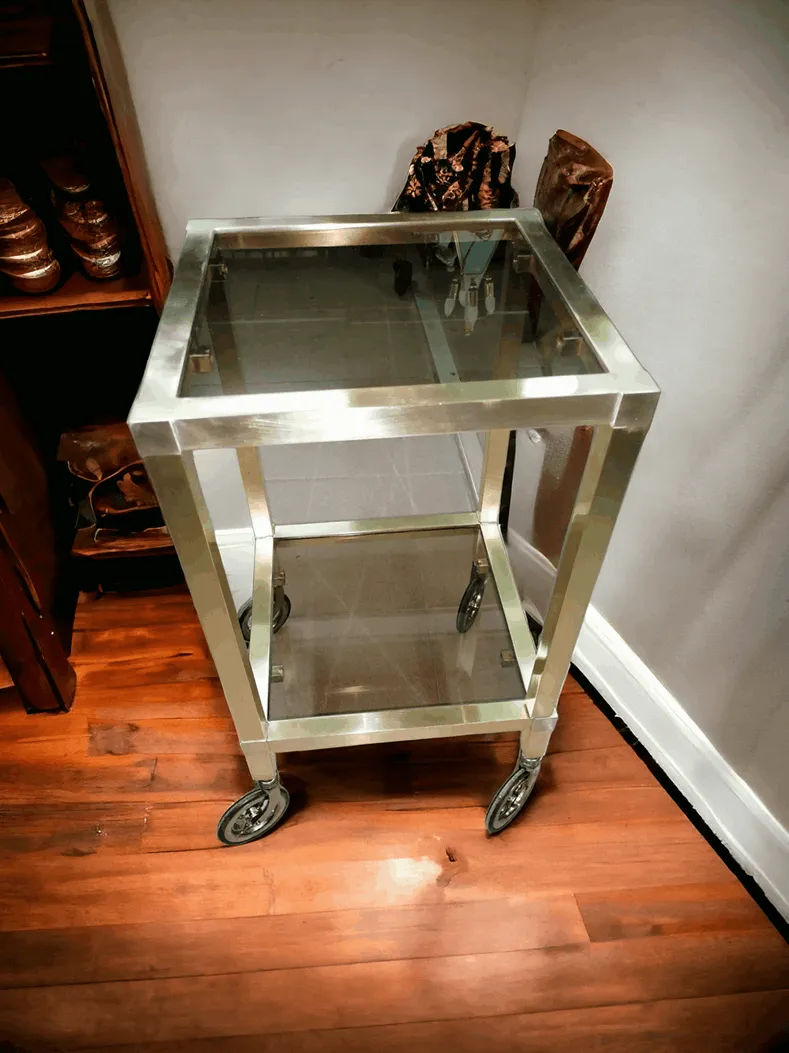 La mesa con ruedas de latón y vidrios es un elegante complemento de decoración que combina practicidad y estilo refinado. Esta mesa tiene una estructura de latón pulido, un material conocido por su atractivo clásico y durabilidad, mientras que los vidrios transparentes aportan ligereza visual y versatilidad. Características principales: Estructura de latón: Las ruedas y los detalles en latón dan un toque de lujo, haciendo que la mesa no solo sea funcional, sino también un elemento decorativo. Vidrios: Las superficies de vidrio transparente permiten exhibir objetos decorativos, manteniendo la habitación luminosa y aireada. Movilidad: Las ruedas añaden practicidad, permitiendo mover fácilmente la mesa para adaptarla a diferentes necesidades y ubicaciones. ¿Por qué elegirla? Esta mesa es ideal para quienes buscan un mueble que combine belleza y funcionalidad. Perfecta para salones elegantes, oficinas o espacios habitables modernos, su diseño refinado enriquece el ambiente con un toque sofisticado y vintage.