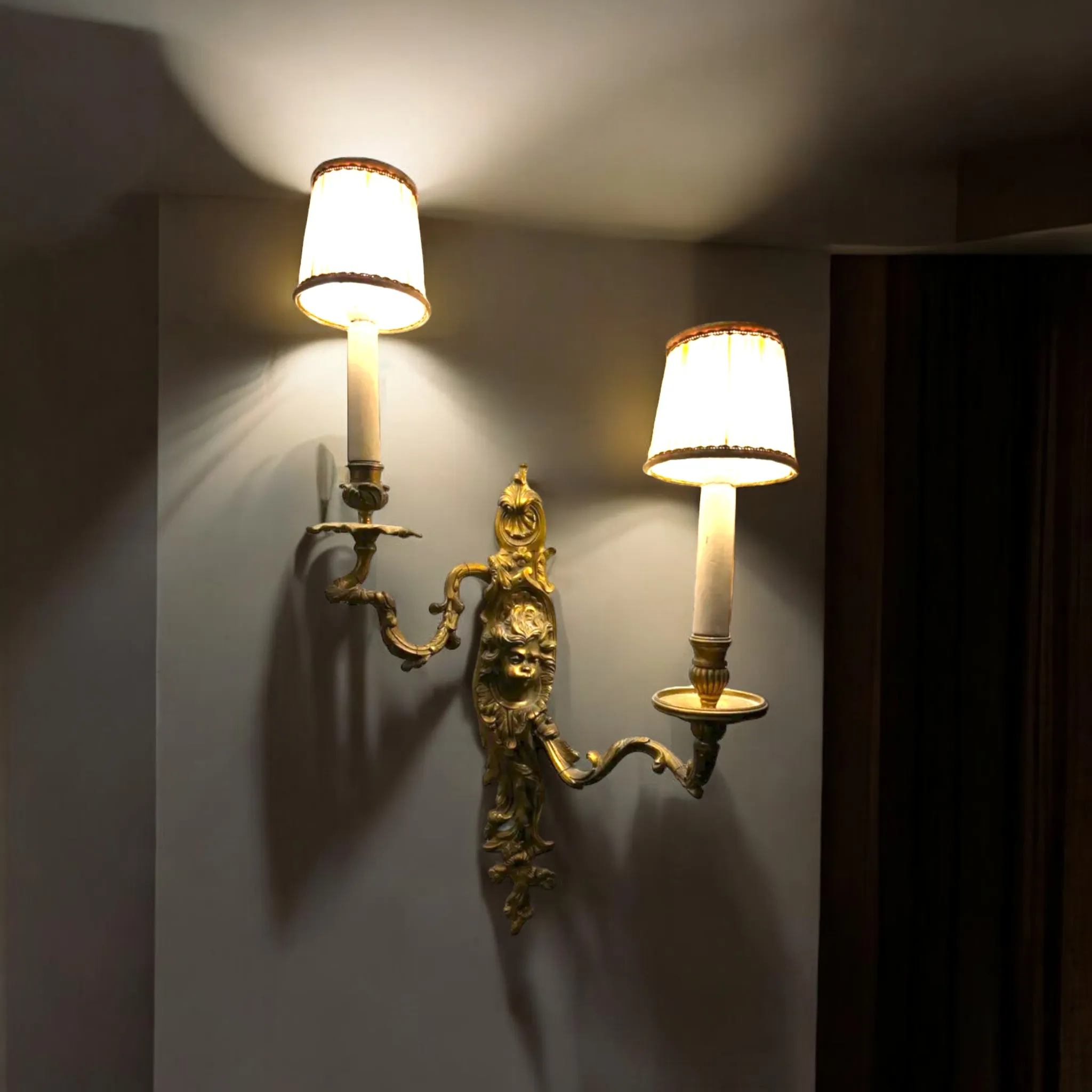 Les appliques en laiton à deux bras avec un putto sont des pièces décoratives raffinées et intemporelles, souvent associées à des styles classiques tels que le Baroque, le Rococo ou le Néoclassique. L'ajout du putto (un petit ange ou figure chérubique) apporte une touche de romantisme et de symbolisme spirituel, typique de l'art décoratif européen. Caractéristiques principales : Matériau : Le laiton est le matériau principal, apprécié pour sa durabilité et sa capacité à développer une patine naturelle avec le temps, ce qui ajoute du charme et de l'authenticité à la lampe. Le laiton peut être poli pour un effet brillant ou laissé vieillir pour un look plus vintage. Design à deux bras : Les deux bras de l'applique s'étendent à partir du corps principal, créant de la symétrie et de l'équilibre. Ces bras ont généralement des lignes courbes et des détails décoratifs tels que des feuilles, des volutes ou de petits motifs floraux. Putto : Le putto est souvent représenté dans une pose ludique ou contemplative, ajoutant un élément figuratif et symbolique à la lampe. Cette figure peut être fusionnée directement dans la structure en laiton ou appliquée séparément comme élément décoratif. Les putti sont un thème récurrent dans l'art et la décoration pour représenter l'innocence, l'amour et la beauté. Installation et Mise en valeur : Ces appliques sont parfaites pour des environnements élégants et de style classique, tels que des salons, des couloirs ou des chambres à coucher. Elles peuvent être montées sur des murs avec des finitions riches ou des tons neutres pour créer un contraste et mettre en valeur les détails en laiton. Entretien et Maintenance : Pour maintenir l'éclat du laiton et la beauté des détails, il est recommandé de nettoyer les appliques avec un chiffon doux et sec. Si le laiton perd son éclat, il peut être poli avec des produits spécifiques, en prenant soin d'éviter les substances abrasives qui pourraient endommager le métal et les détails sculptés du putto. Ce type d'applique est un excellent choix pour ceux qui aiment les pièces de mobilier ayant une forte référence historique et artistique, et peut être considéré comme un investissement de valeur s'il est bien conservé.