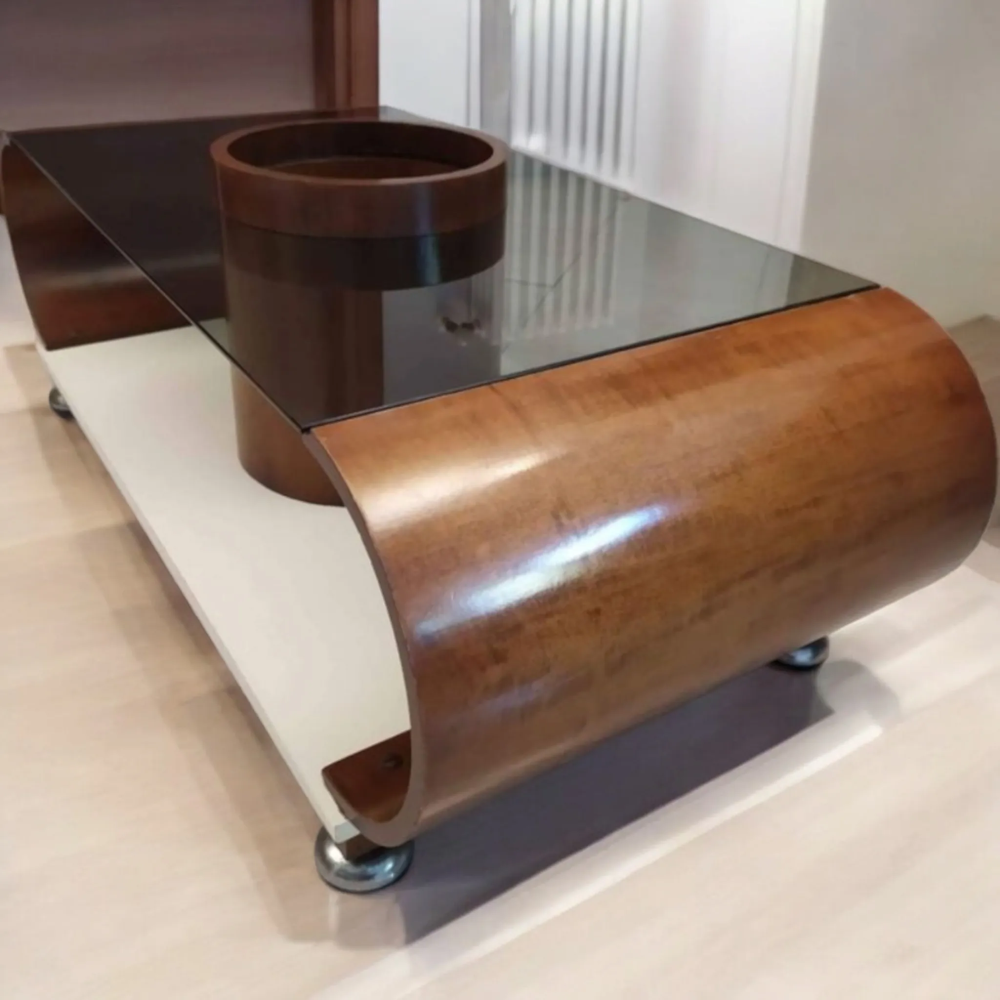 La mesa curvada para licor redonda central estilo Joe Colombo representa una fusión perfecta de diseño moderno y funcionalidad. Inspirada en el trabajo innovador del célebre diseñador italiano Joe Colombo, esta mesa no es solo un complemento de mobiliario, sino una verdadera obra de arte, pensada para combinar estética y practicidad de manera elegante. Características principales: Diseño curvado: La mesa presenta líneas suaves y fluidas, típicas del estilo de Joe Colombo, que resalta la simplicidad y la modernidad. Las curvas armoniosas del mueble lo convierten en una pieza dinámica y fascinante. Funcionalidad para licor: Con su compartimento central destinado al almacenamiento de botellas y accesorios para licor, la mesa no solo sirve como una pieza elegante para el salón, sino que también ofrece una solución práctica para alojar y servir bebidas. Estilo Joe Colombo: Famoso por su capacidad de crear objetos funcionales sin comprometer el diseño, Colombo introdujo soluciones innovadoras que combinan forma y función de manera perfecta. La mesa para licor es un claro ejemplo de su visión única. ¿Por qué elegirla?: Esta mesa es ideal para quienes buscan un mueble que combine la elegancia del diseño italiano contemporáneo con la practicidad de la organización. Perfecta para salones modernos o espacios de entretenimiento, no solo decora, sino que también añade un toque de clase a tu hogar. La mesa estilo Joe Colombo es una elección perfecta para quienes aprecian el diseño funcional y para aquellos que desean un mueble que se distinga por su originalidad y estilo.
