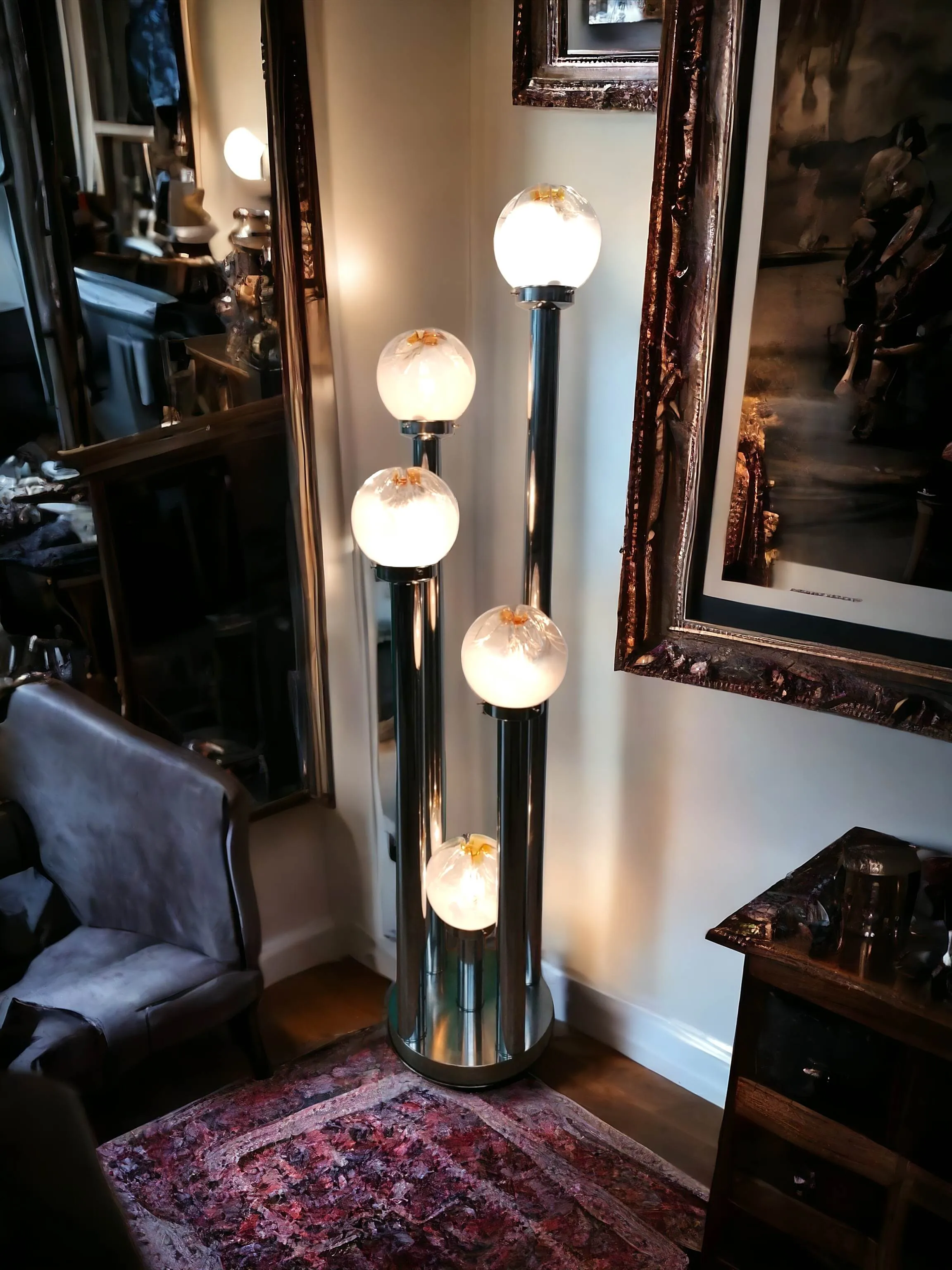 Cette lampe sur pied Murano, conçue par Toni Zuccheri pour VeArt, incarne l’élégance raffinée du design italien des années 70. Avec cinq globes lumineux en verre de Murano, chaque point lumineux renferme des détails uniques, avec des nuances dorées et des formes organiques qui rappellent la chaleur de la lumière naturelle. Les structures chromées verticales apportent une touche moderne et industrielle, équilibrée par le charme artisanal du verre soufflé. Parfaite pour mettre en valeur un coin du salon ou un espace de détente, cette lampe n’est pas seulement une source de lumière, mais une véritable œuvre d’art, capable d’enrichir tout environnement d’une atmosphère sophistiquée et intemporelle.