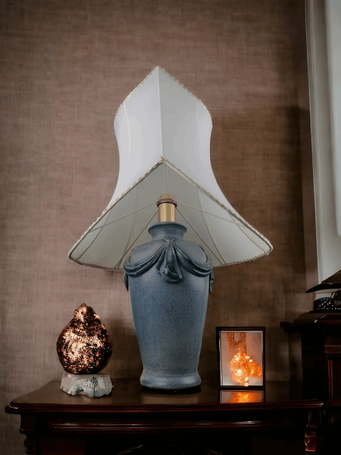 Cette majestueuse lampe de table de style Art Nouveau combine un design raffiné et des détails soignés pour capturer l'essence du mouvement artistique de la fin du XIXe siècle. La base en céramique bleue, aux lignes douces et décorée de drapés sculptés, évoque l'élégance organique typique de ce style. L'abat-jour, d'une forme originale et sinueuse, diffuse une lumière tamisée qui met en valeur les détails du mobilier environnant, créant une ambiance chaleureuse et accueillante. Parfaite pour ajouter une touche de charme vintage et une présence scénique à tout environnement, cette lampe est une déclaration de style et de bon goût.