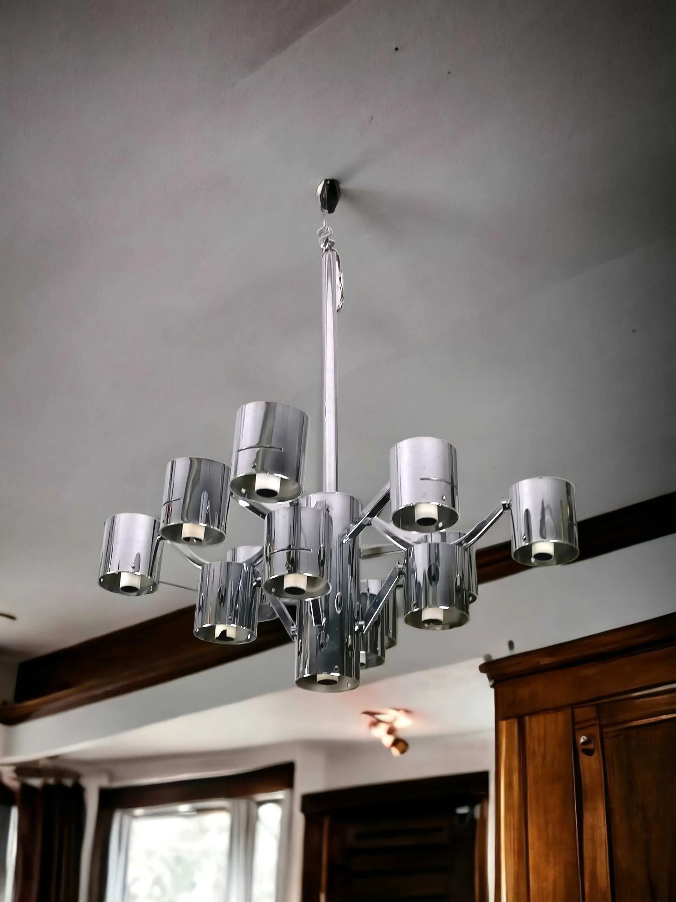 Ce lustre est vraiment fascinant ! La structure en acier et le design géométrique avec les cylindres réfléchissants rappellent beaucoup le travail de Gaetano Sciolari, connu pour ses créations d'éclairage de luxe dans les années 60 et 70. Sciolari utilisait souvent des formes géométriques et des matériaux comme le chrome pour créer un effet futuriste et sculptural, ce qui rend cette attribution très plausible.