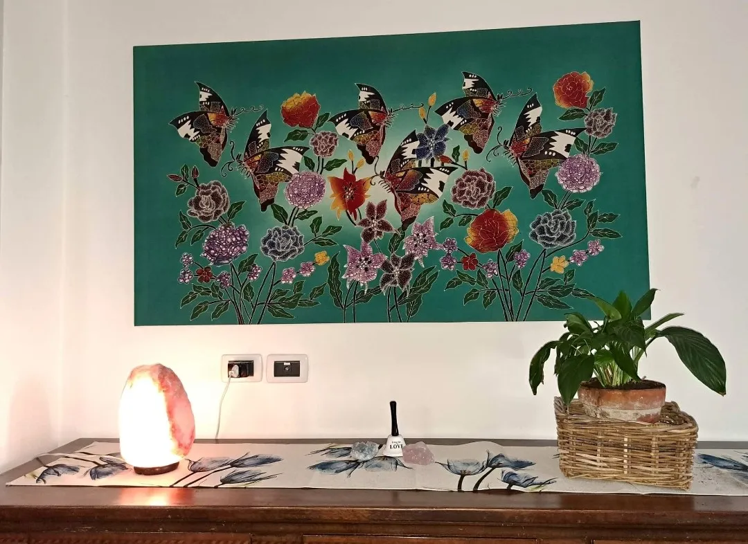 一幅描绘蝴蝶图案的丝绸大Batik画作，是将传统的丝绸绘画与Batik技法相结合的艺术品。Batik是一种使用蜡在织物上创作图案和设计的染色方法，起源于印度尼西亚，以其精美的图案和丰富的色彩而闻名。主要特点：蝴蝶图案：蝴蝶象征着转变、轻盈与美丽，其形态精致、色彩鲜艳，通过技法展示。每只蝴蝶色彩斑斓，象征着深刻的含义。Batik技法：Batik技法利用蜡的特殊效果，创造出清晰的细节，背景则较为深沉或彩色。每幅画都经过精心设计，突出了丝绸的自然色调，增添了深度和动感。材料：丝绸是Batik工艺的理想选择，它能很好地吸收颜色，赋予画作独特的光泽感。此外，丝绸还增添了一份优雅与精致，使画作成为一件高雅的展览品。为什么选择这幅蝴蝶Batik画？这幅蝴蝶图案的大尺寸丝绸Batik画是寻求一件能够增添优雅和轻盈感的艺术作品的理想选择。凭借丝绸本身的美丽和Batik工艺的精湛，这幅画不仅是一种装饰，更是艺术表达的真实体现，能够使任何空间焕发高贵气息。蝴蝶图案更增添了一份宁静与自然之美。