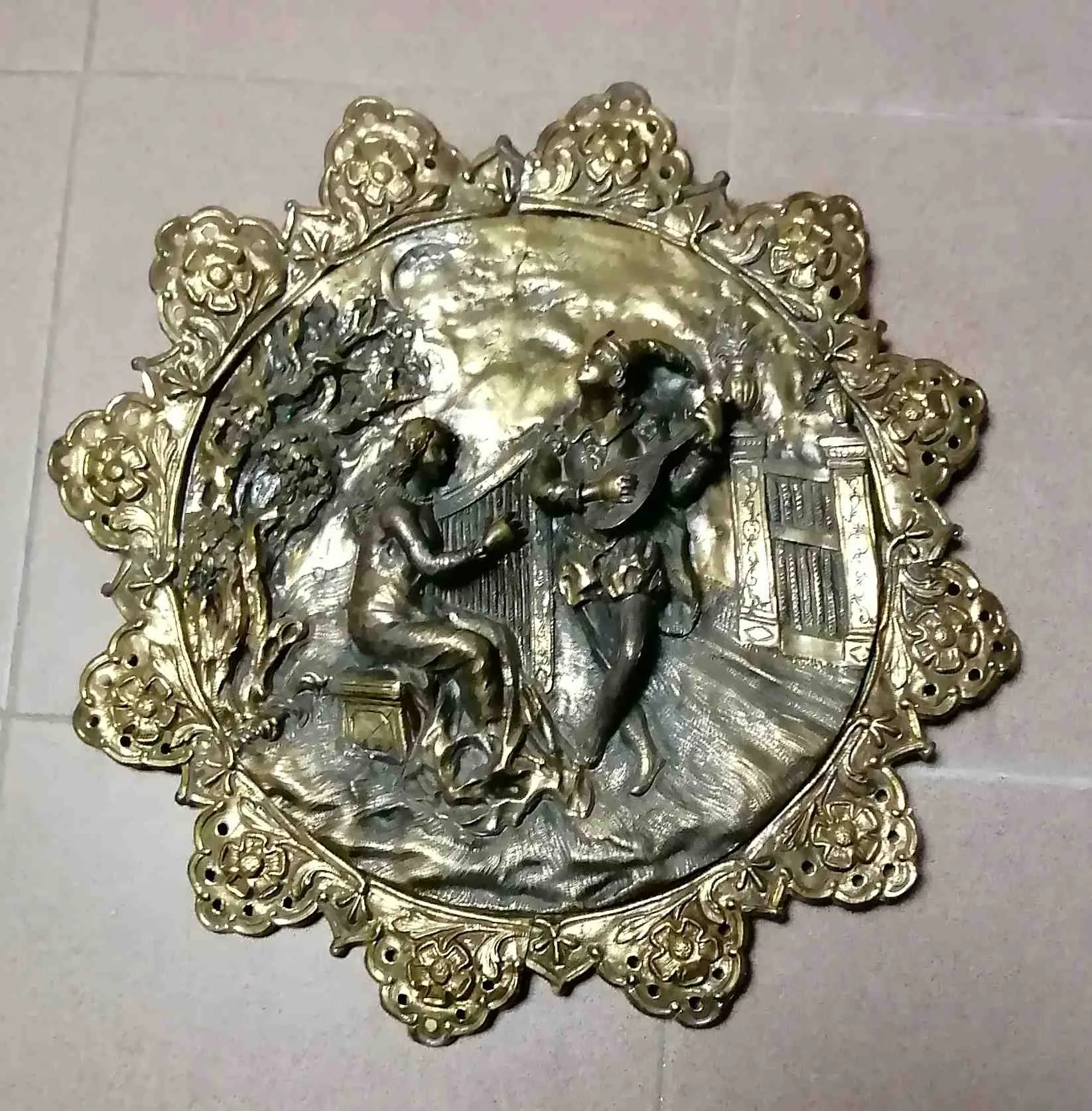 这只青铜浮雕盘描绘了音乐家和游吟诗人的场景，是一件迷人的艺术作品，庆祝了音乐的喜悦和表演艺术。这件作品不仅作为装饰元素，还代表了一个过去时代的音乐和艺术文化的重要见证。材质与技艺：这只青铜盘采用浮雕工艺，传统的金属塑形技术，创造出浮雕和三维形态。这种技艺增强了细节表现，让描绘的主题栩栩如生，使这只盘子成为一件视觉丰富、迷人的作品。音乐家的呈现：盘中的场景描绘了几位音乐家，其中包括一位游吟诗人，唤起了节庆和庆典的氛围。音乐家们常常被描绘成演奏传统乐器，如琵琶或长笛，捕捉到音乐瞬间的动感和能量。游吟诗人通常被突出表现，姿态生动，传达了音乐的激情与欢乐。视觉冲击与背景：这只盘子不仅仅是一个装饰物，它对于那些对音乐史和艺术感兴趣的人来说，是一个重要的研究元素。它可以被展示在庆祝文化和传统的环境中，作为宾客之间的对话话题。它吸引注意力并激发兴趣，适合收藏家和装饰艺术爱好者。为什么选择一只描绘音乐家的青铜浮雕盘？