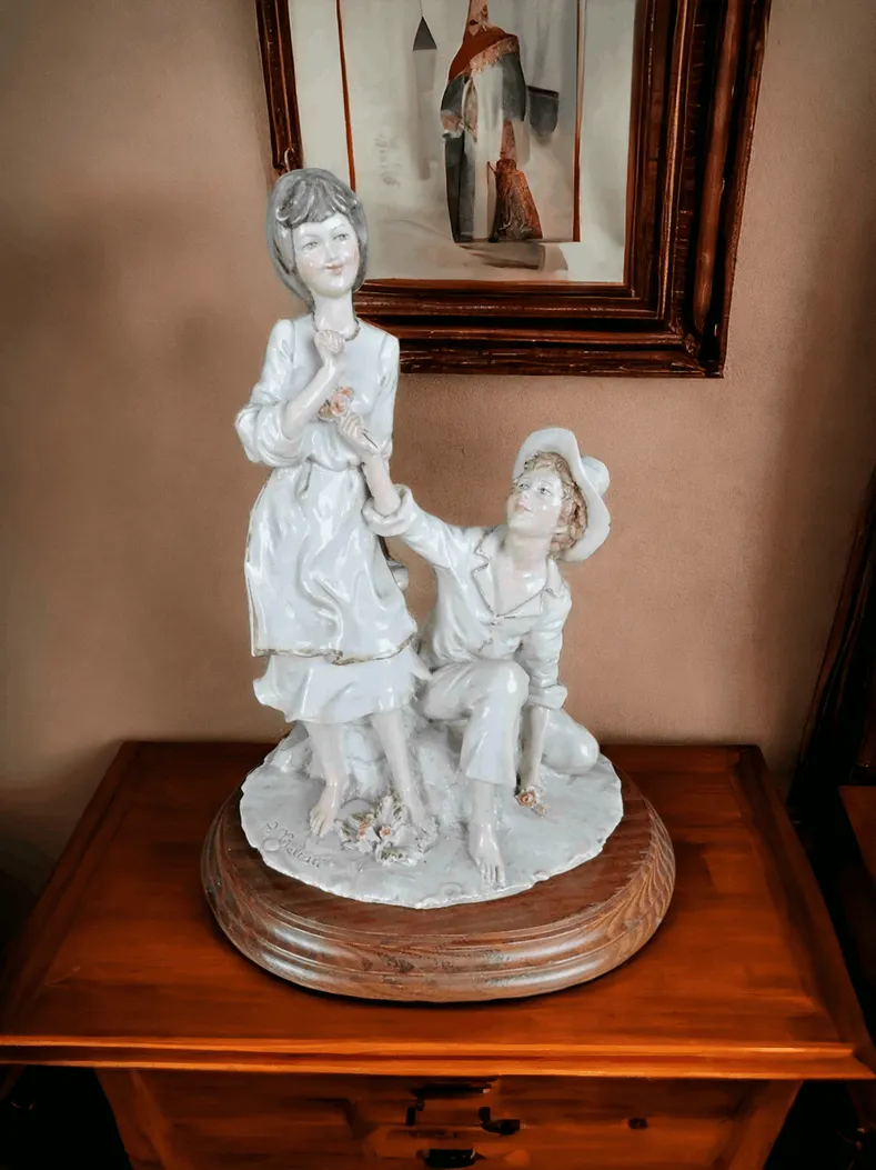 这款Capodimonte《恋爱中的年轻人》雕像由A. Belcari签名，是一件精致的瓷器艺术品，体现了Capodimonte制造厂的传统和精致工艺，因其精美且极具细节的作品而闻名。此雕像是爱的象征，描绘了一对年轻恋人，在亲密的瞬间，可能是一个吻或一个温柔的拥抱。材质与工艺：该雕像采用高档瓷器制作，表面具有典型的光泽感和柔和质感，展现了Capodimonte制作的优质作品。雕像表面经过精细雕刻，特别是面部表情和衣物褶皱，细节处理非常精致。A. Belcari的签名增添了艺术价值，突出其与这位才华横溢的艺术家的联系。设计与细节：雕像表现的是一对恋爱中的年轻人，极具浪漫气息，适合在优雅的环境中展示。雕像的姿势和面部表情旨在传达细腻的爱意，带给人一种温柔与亲切的感觉。装饰细节，如精致的发型、雕刻精美的衣物和配件，凸显了工匠对瓷器艺术的巧妙雕刻技艺。艺术价值：由A. Belcari签名的这件雕像，也是20世纪意大利雕塑艺术的重要代表之一。恋爱中的年轻人这一主题一直以来都是艺术家们的创作灵感源泉。细致的雕刻工艺与Capodimonte瓷器的优质结合，使这件雕像成为艺术爱好者和收藏家的珍品。展示位置与用途：这件雕像非常适合摆放在展示柜、桌面或客厅书架上。其优雅的造型使其成为浪漫礼物或精美家居装饰的理想选择，象征着爱与美的永恒。